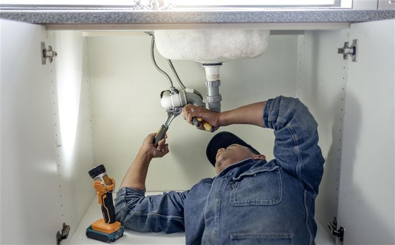Plumber repairing pipes beneath a bathroom sink in Vacaville